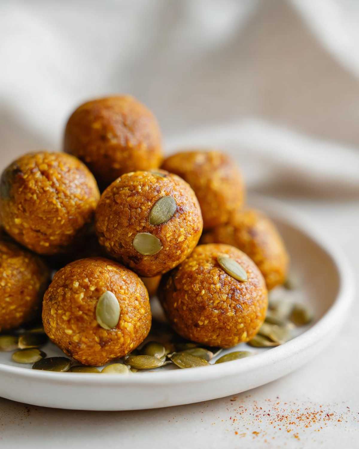 A close-up of delicious pumpkin protein bites topped with pumpkin seeds, arranged on a white plate with scattered pumpkin seeds.