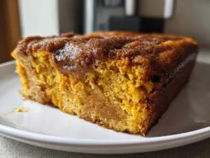A close-up view of a moist slice of pumpkin snickerdoodle snack cake on a white plate.