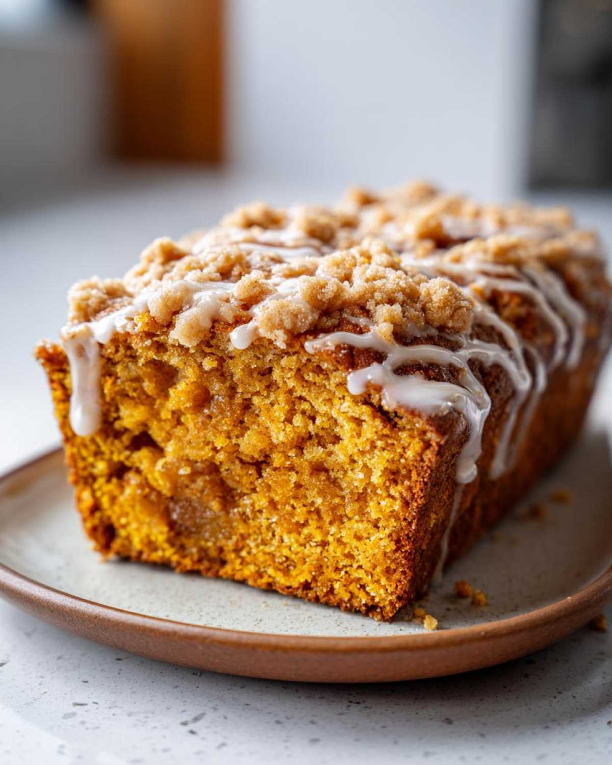 A close-up of a moist pumpkin streusel bread loaf drizzled with a sweet glaze.