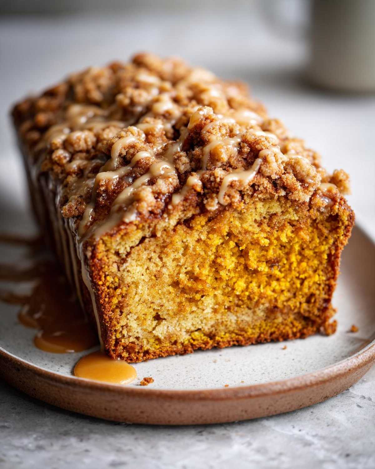 A slice of moist pumpkin streusel bread topped with a sweet glaze and streusel crumble, served on a plate.