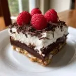 A decadent slice of raspberry chocolate lasagna topped with whipped cream, chocolate shavings, and fresh raspberries.