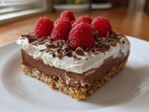 A slice of raspberry chocolate lasagna topped with whipped cream, fresh raspberries, and chocolate shavings.