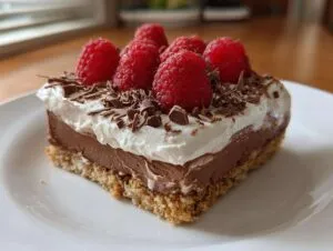 A slice of raspberry chocolate lasagna topped with whipped cream, fresh raspberries, and chocolate shavings.