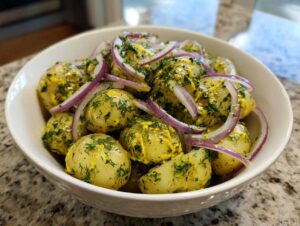 A bowl of creamy Scandinavian dill potato salad topped with fresh dill and thinly sliced red onion.