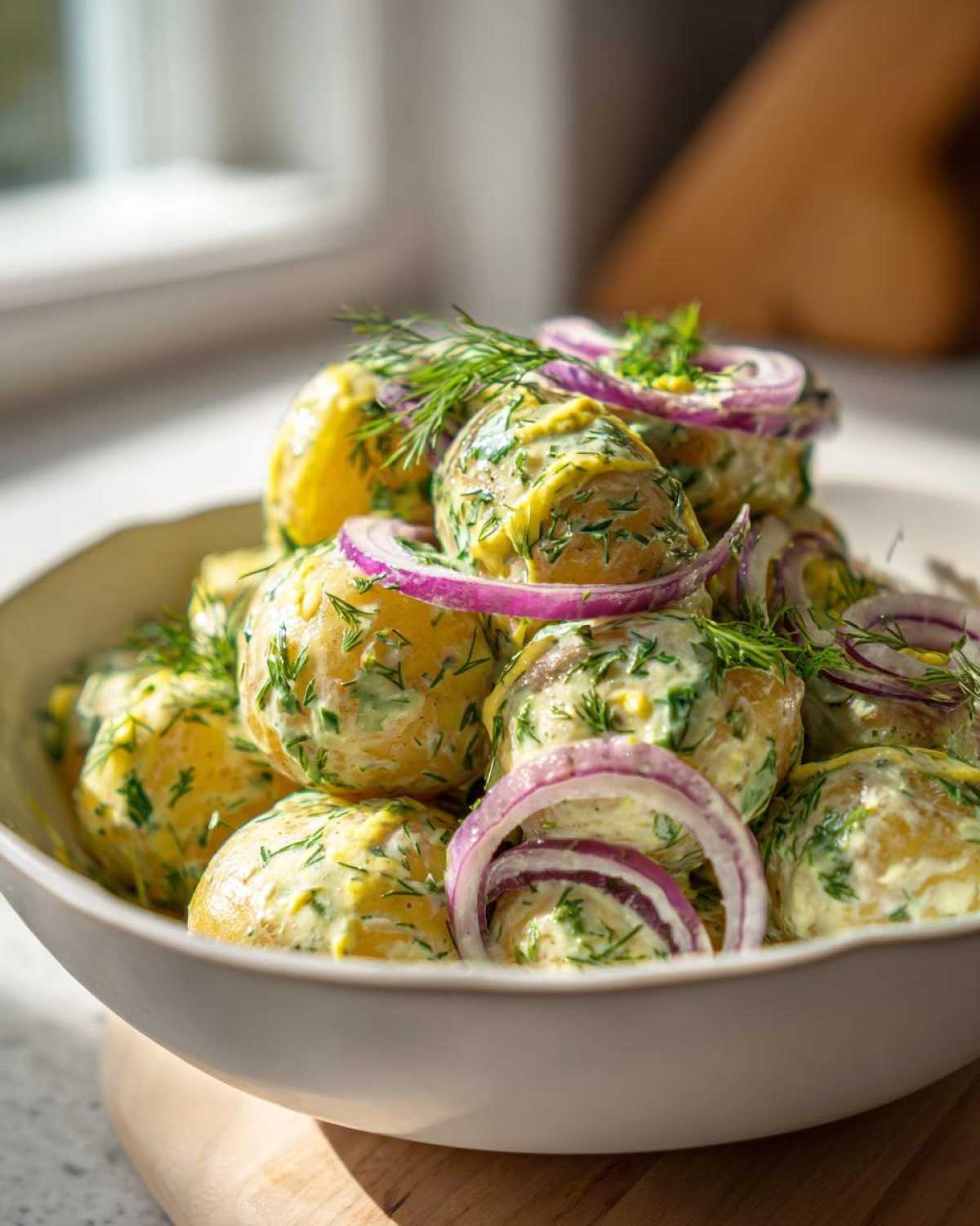 A close-up of creamy Scandinavian dill potato salad in a bowl, garnished with red onion rings and fresh dill.
