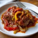 A close-up of tender smothered swiss steak topped with a rich tomato sauce, onions, and bell peppers.