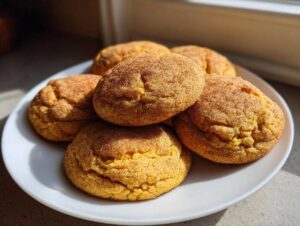 A pile of soft and chewy pumpkin cookies dusted with cinnamon sugar on a white plate.