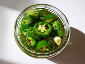 Close-up overhead view of bright green pickled jalapeños with garlic cloves in a glass jar.