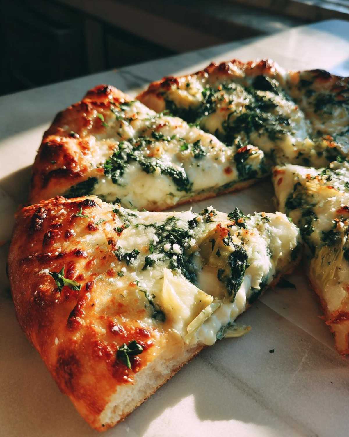 A close-up of a slice of spinach artichoke pizza, showcasing melted cheese, spinach, and artichoke hearts.