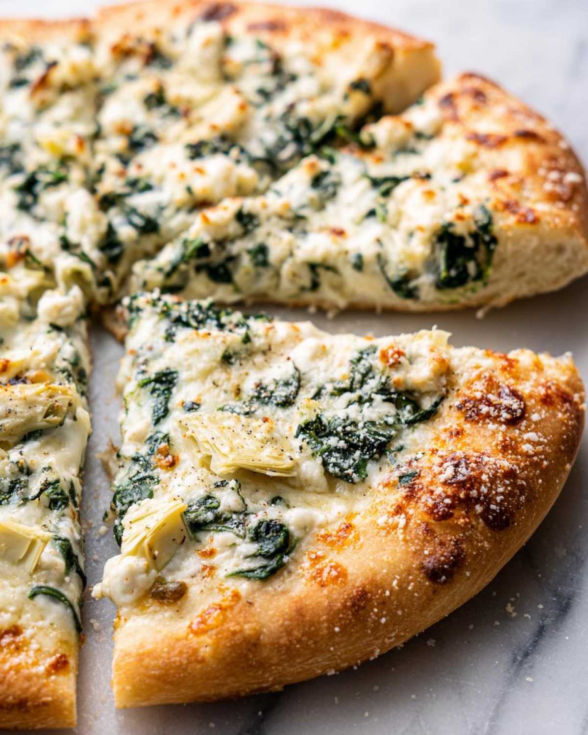 A close-up shot of a slice of spinach artichoke pizza, showcasing the creamy cheese, spinach, and artichoke toppings on a golden crust.
