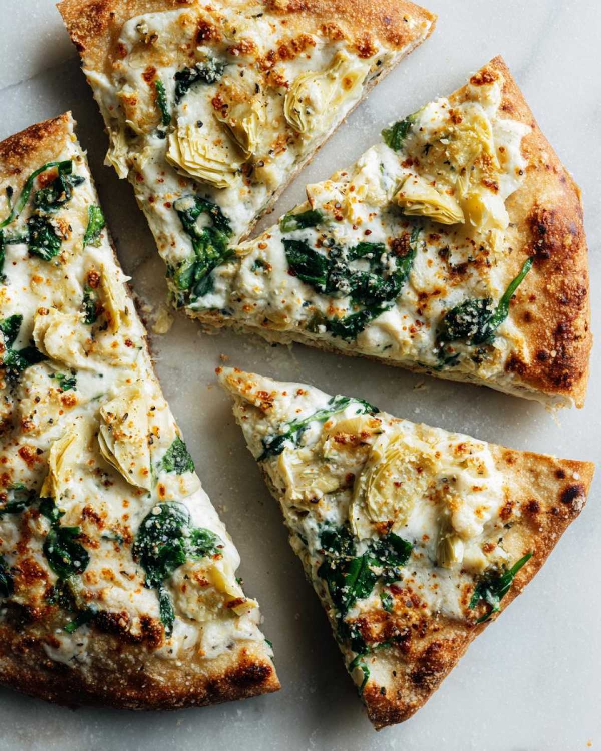 Close-up of four slices of spinach artichoke pizza, showcasing the creamy white sauce, green spinach, and artichoke hearts.