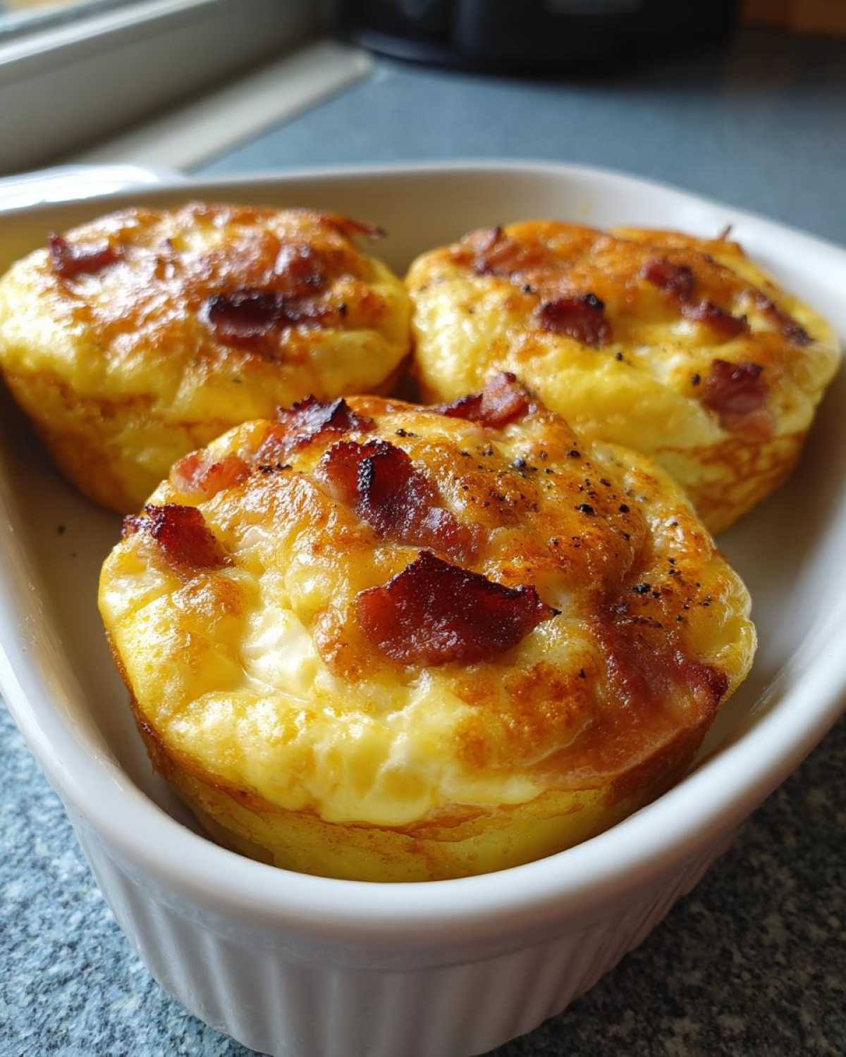 Three creamy Starbucks egg bites topped with crispy bacon in a white dish.