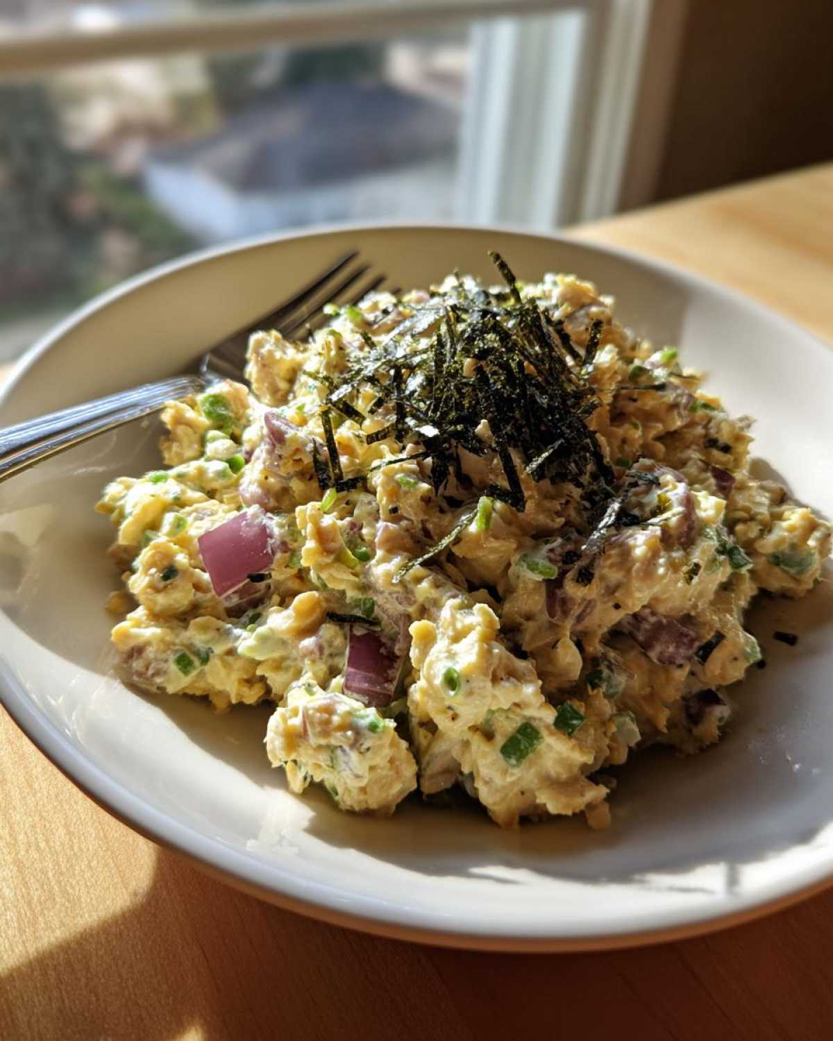 A close-up of a bowl filled with vegan chickpea tuna salad, topped with shredded nori.