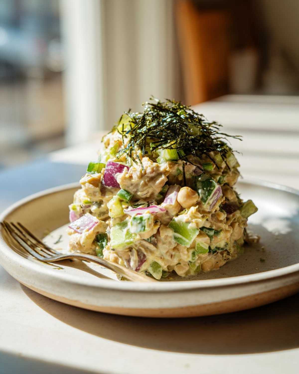 A mound of vegan chickpea tuna salad topped with nori flakes, served on a plate with a fork.
