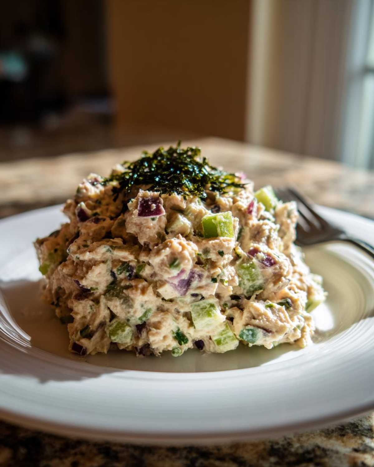 A close-up of a generous portion of vegan chickpea tuna salad, topped with shredded seaweed, on a white plate.