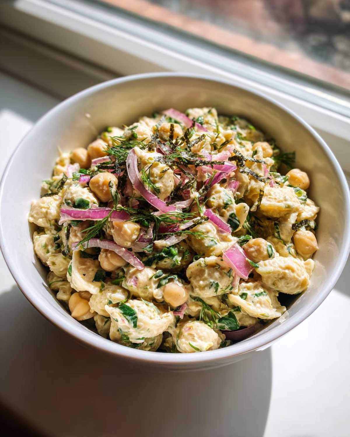 A bowl of creamy vegan tuna pasta salad with chickpeas, red onion, and dill.