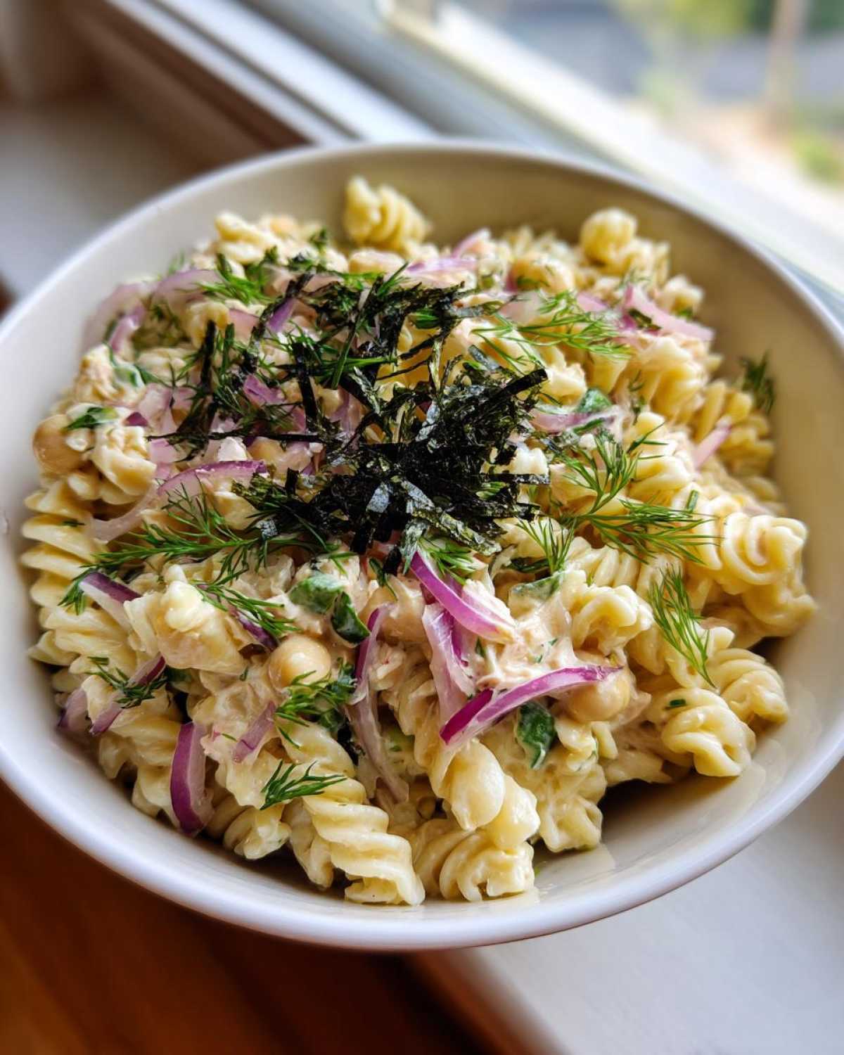 A bowl of creamy vegan tuna pasta salad with fusilli pasta, chickpeas, red onion, dill, and nori flakes.
