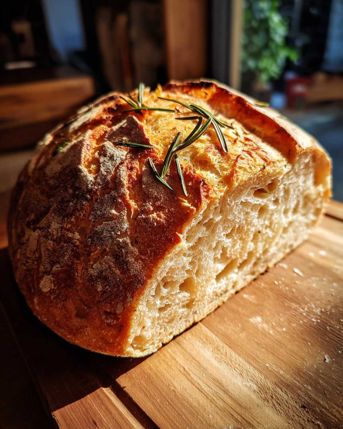 A rustic loaf of whole wheat rosemary bread, sliced in half, showcasing its airy crumb and golden crust.