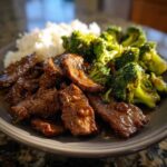 A close-up of a plate of tender beef and broccoli stir-fry served with white rice.