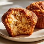 Close-up of a delicious apple cinnamon muffin, with a bite taken out, revealing soft interior and apple chunks.
