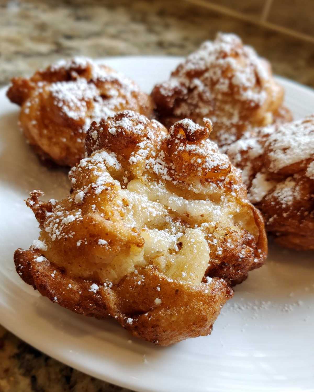 Close-up of golden brown baked apple fritters dusted with powdered sugar on a white plate.