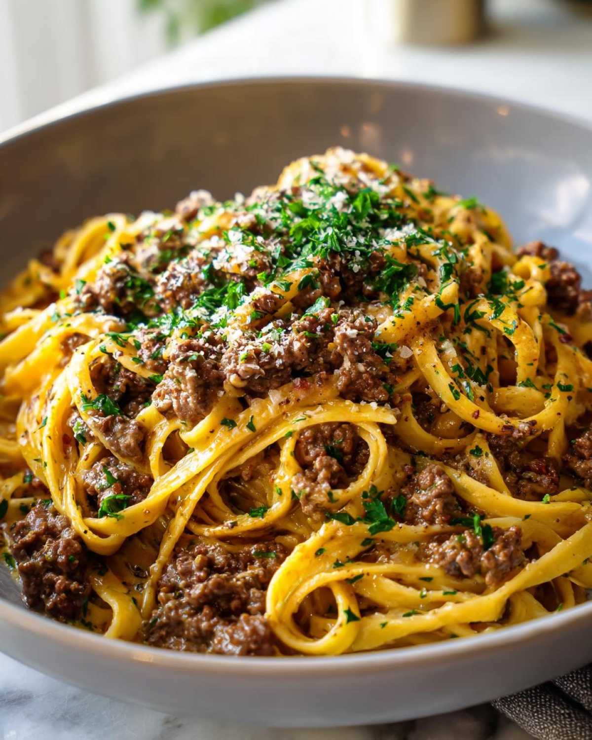 A close-up of a bowl of Beef and Garlic Butter Linguine, topped with fresh parsley and grated cheese.