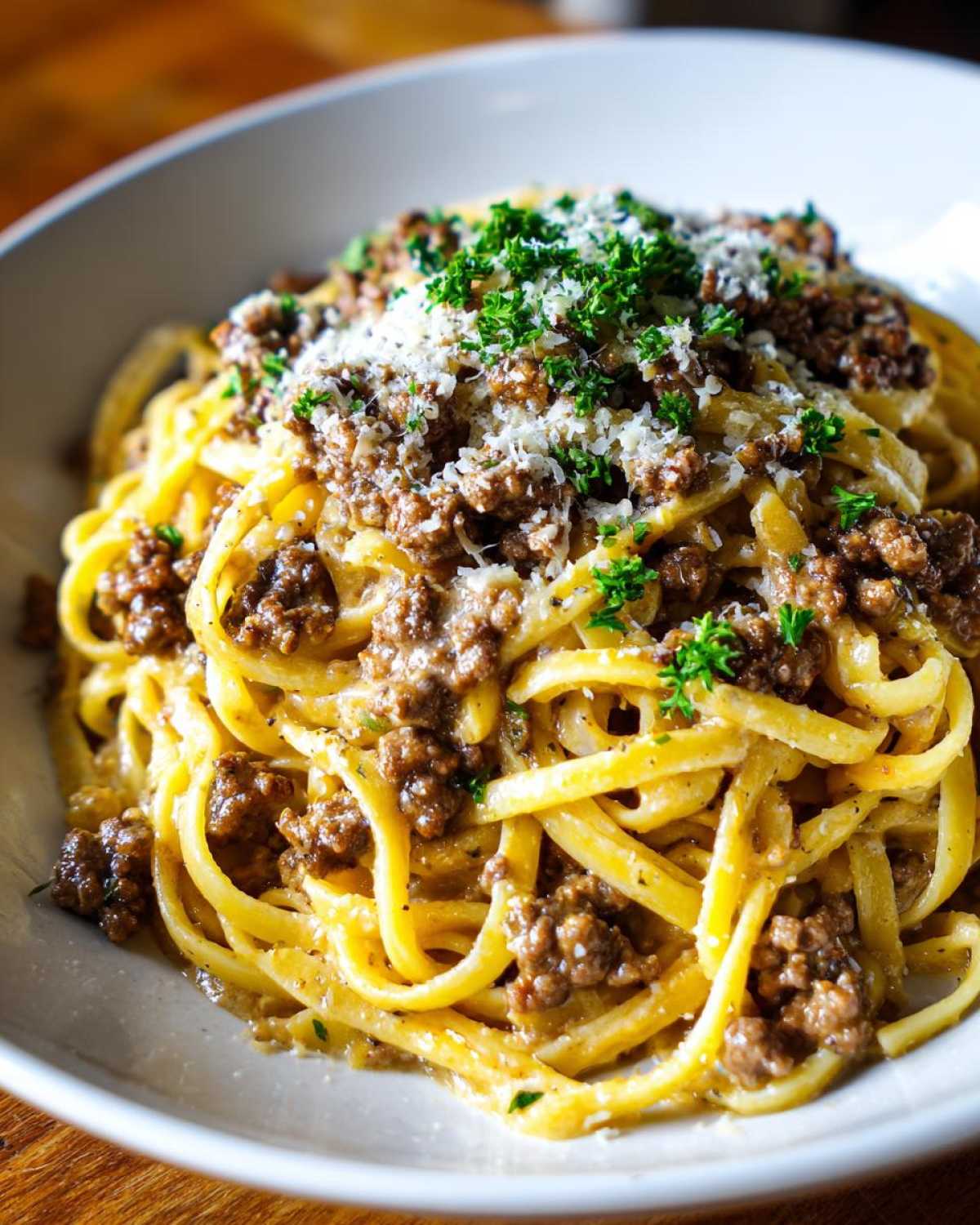 A close-up of a bowl of Beef and Garlic Butter Linguine, topped with minced beef, grated cheese, and fresh parsley.