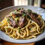 A close-up of a white bowl filled with beef garlic butter linguine, topped with sliced steak, grated cheese, and fresh parsley.