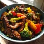 A close-up of a bowl filled with juicy beef stir fry, featuring tender beef strips, vibrant broccoli florets, and colorful bell peppers.
