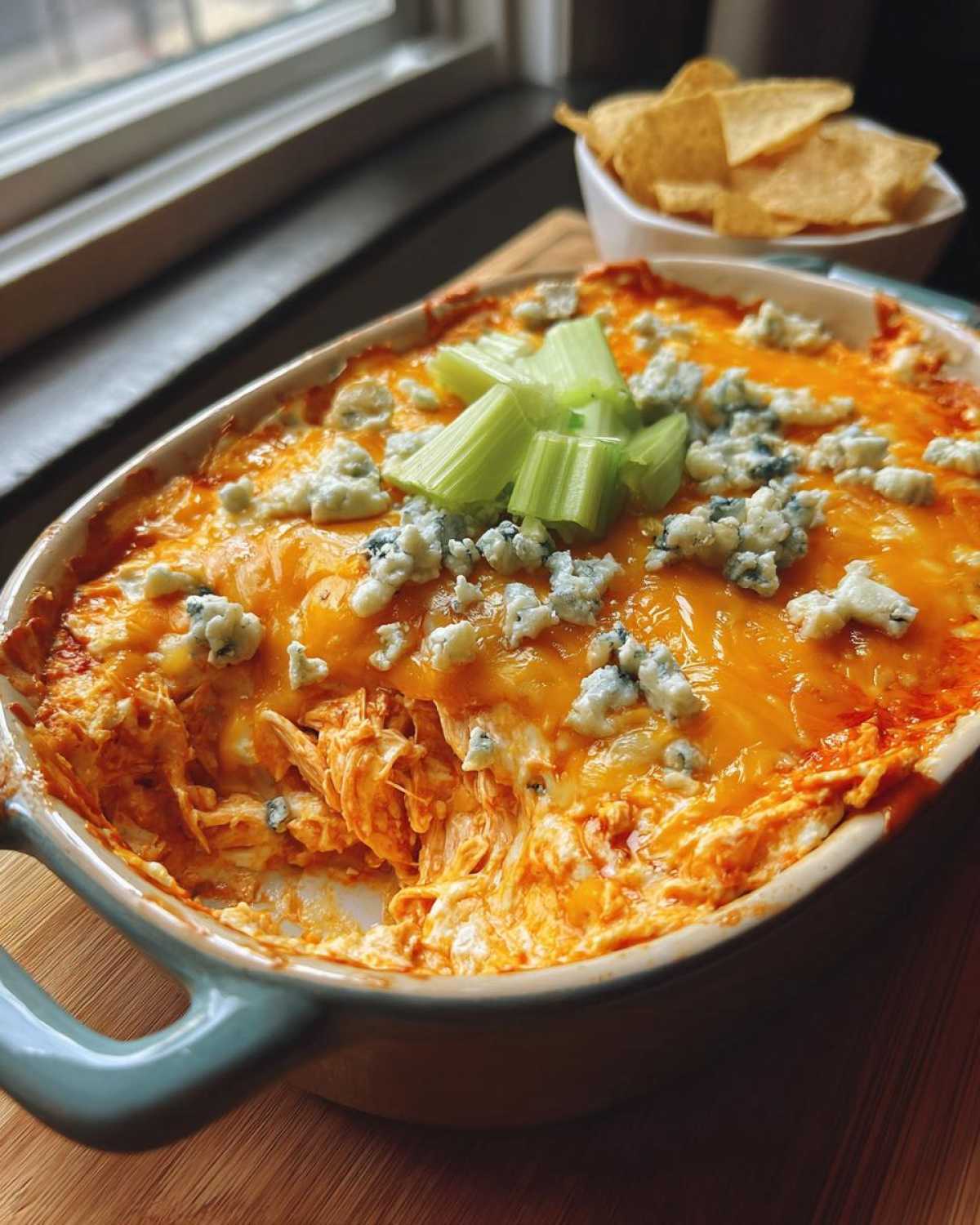 A bubbling hot dish of classic Buffalo chicken dip, topped with melted cheese, blue cheese crumbles, and fresh celery sticks.