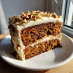 A slice of moist carrot cake layered with rich cream cheese frosting and topped with chopped walnuts.