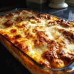 Close-up of a bubbly, golden-brown cheesy baked spaghetti casserole in a glass baking dish.