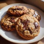 Close-up of several chewy chocolate chip cookies piled on a white plate, with large chocolate chunks visible.