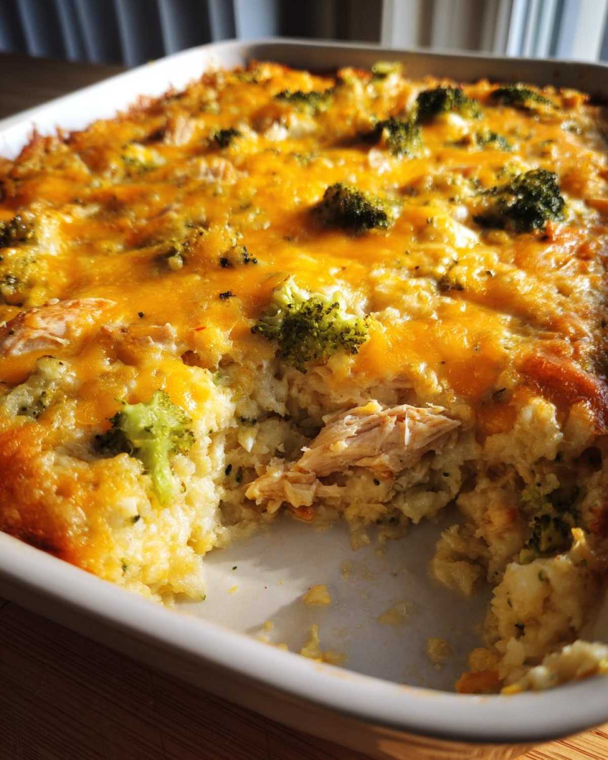 A close-up of a creamy chicken cauliflower rice casserole topped with melted cheddar cheese and broccoli florets.