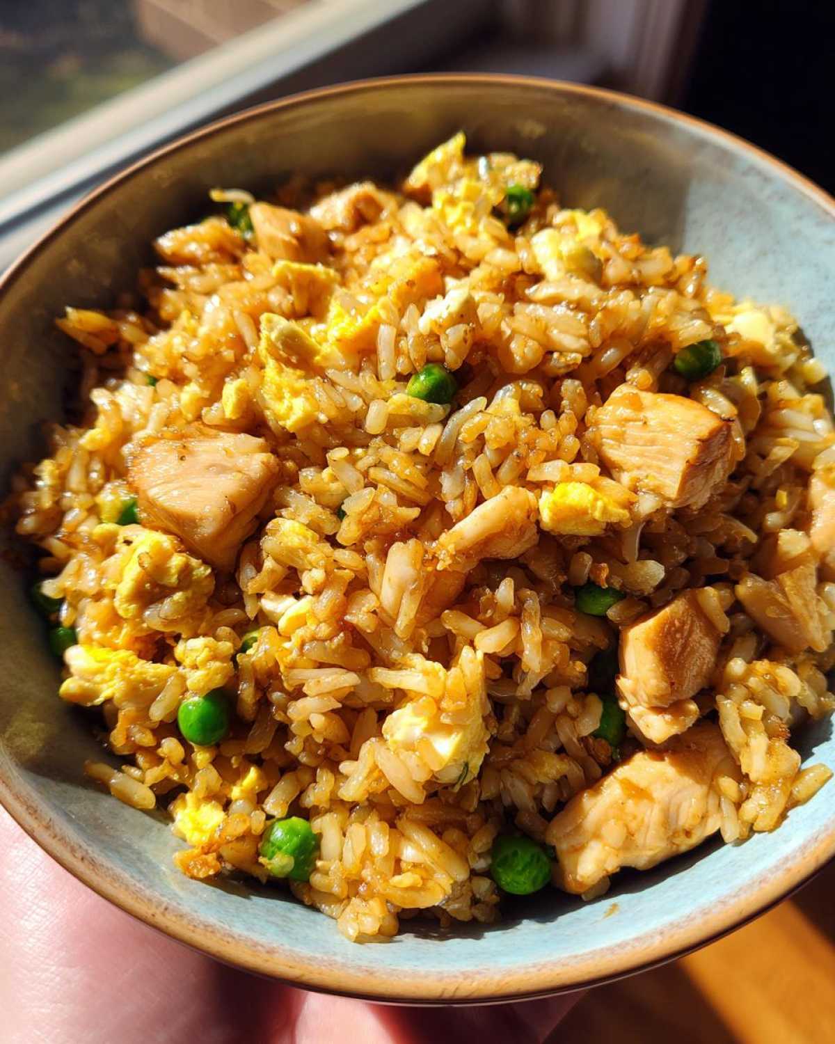 A close-up of a bowl filled with savory chicken fried rice, featuring tender chicken pieces, scrambled eggs, and peas.