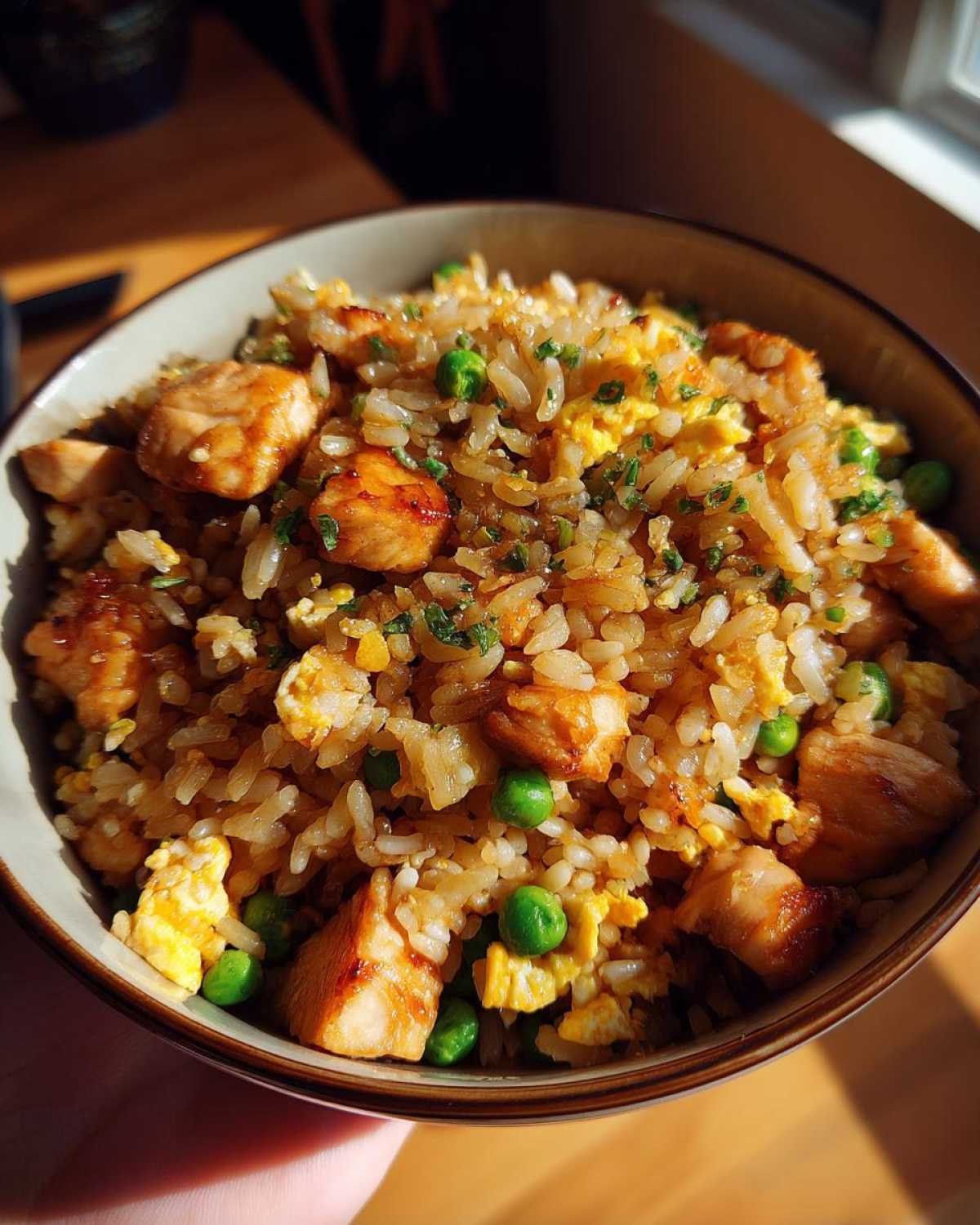 A close-up of a bowl of homemade chicken fried rice with peas and scrambled eggs, garnished with parsley.