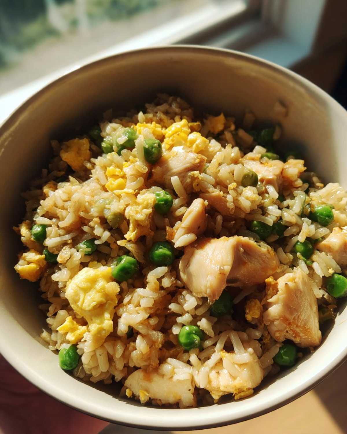 Close-up of a bowl filled with appetizing chicken fried rice, featuring tender chicken pieces, scrambled eggs, and bright green peas.