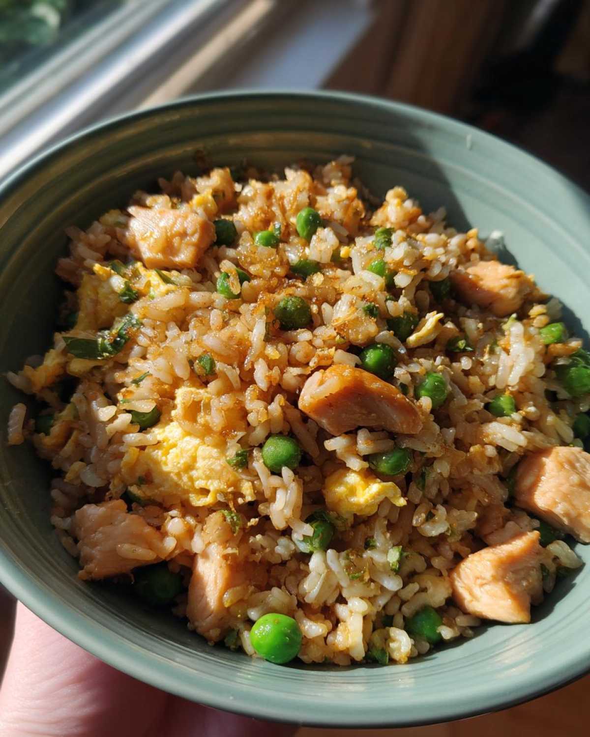 A close-up shot of a bowl of homemade chicken fried rice with peas and scrambled egg.