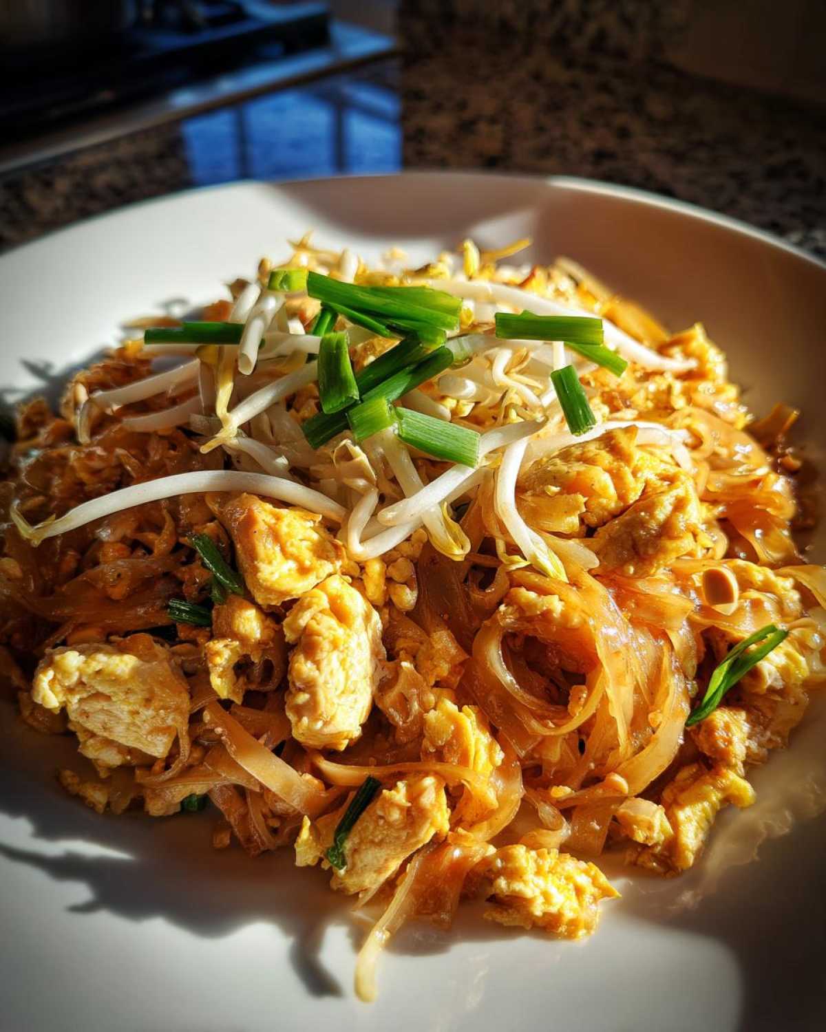Close-up of a plate of Chicken Pad Thai, featuring rice noodles, scrambled egg, chicken pieces, bean sprouts, and chopped green onions.