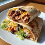 A delicious Chipotle Ranch Grilled Chicken Burrito, cut in half, revealing seasoned chicken, rice, black beans, cheese, and lettuce.