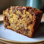 A close-up of a moist slice of chocolate chip banana bread on a plate, showcasing melted chocolate chips.
