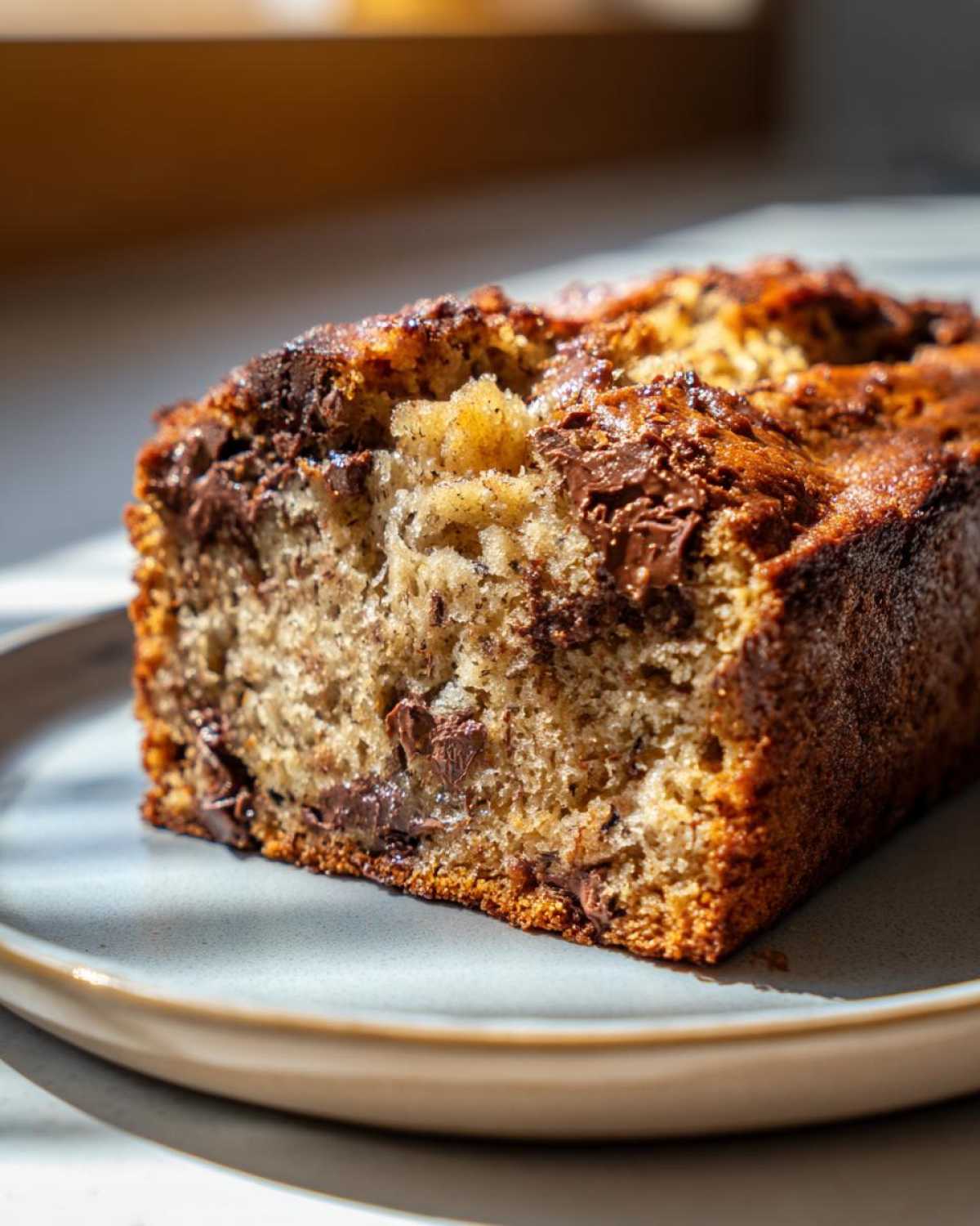 Close-up of a slice of ultra-moist chocolate chip banana bread on a plate, showcasing melted chocolate chips.