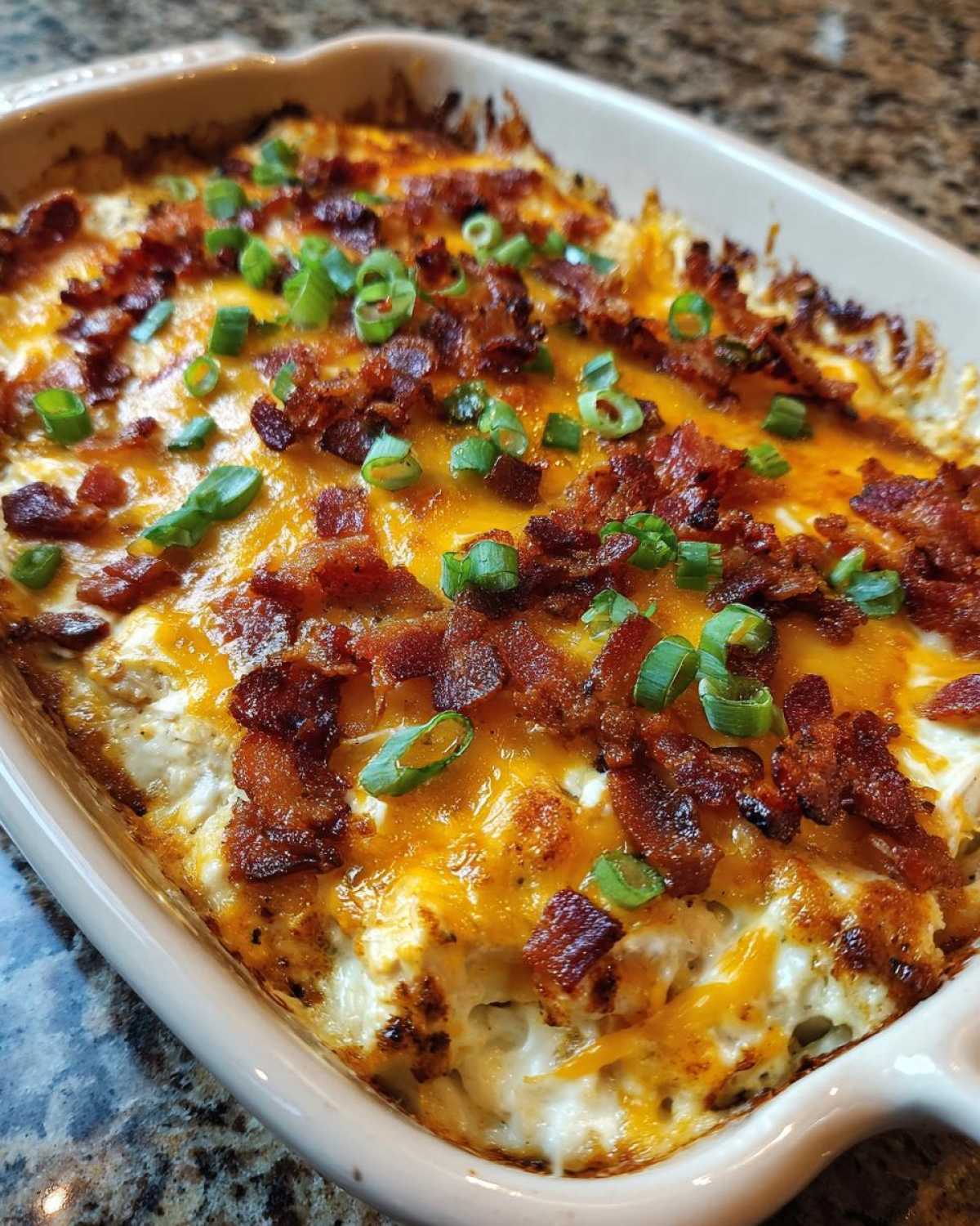 Close-up of a baked crack chicken casserole topped with melted cheddar cheese, crispy bacon bits, and chopped green onions.
