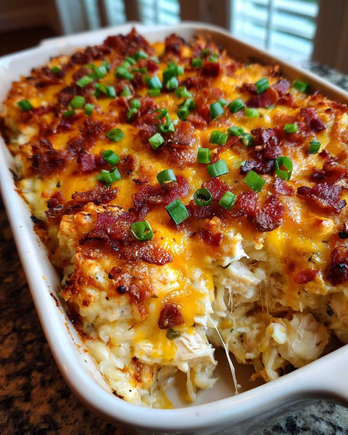 Close-up of a bubbling Crack Chicken Casserole topped with melted cheddar cheese, crispy bacon, and green onions.
