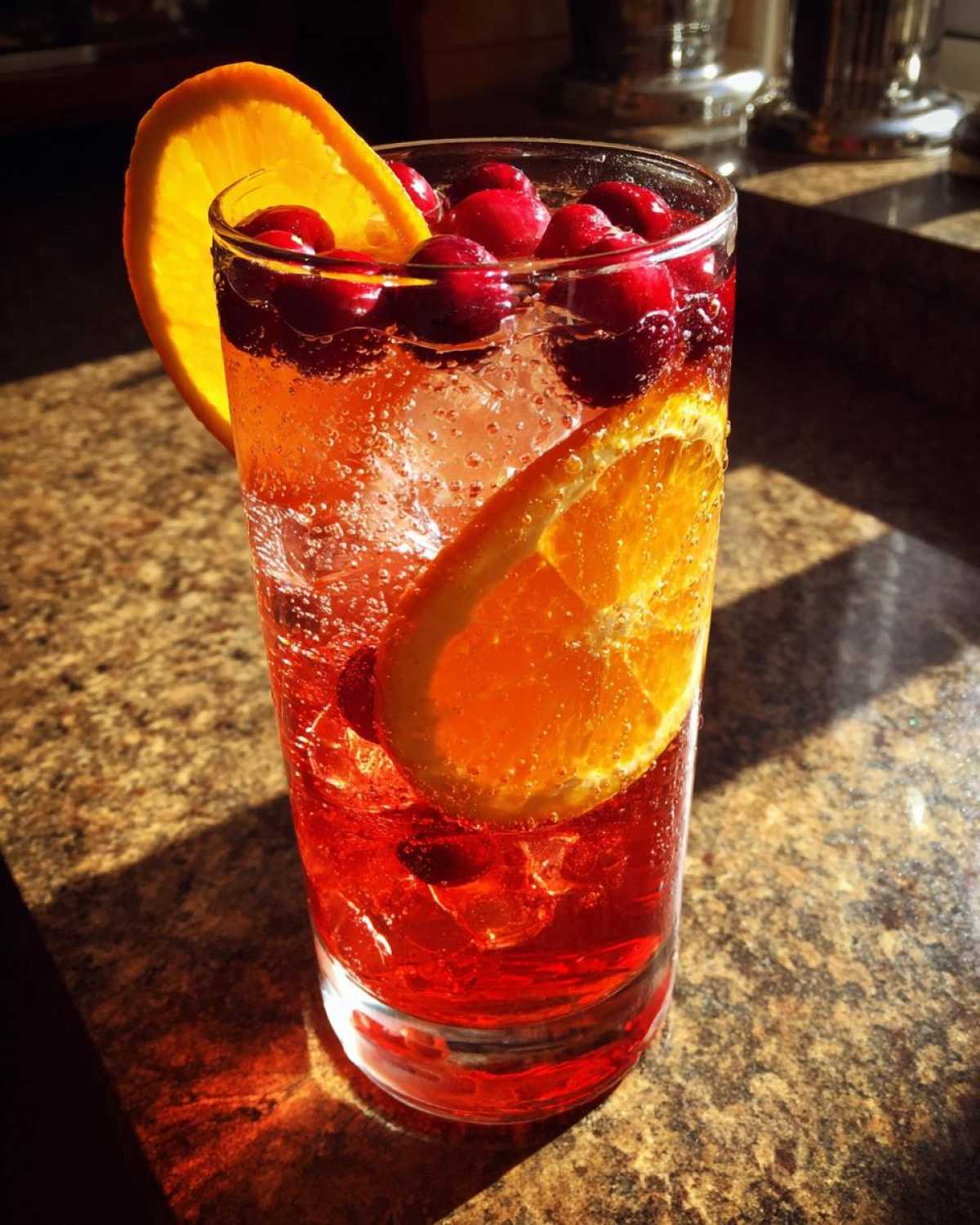 A tall glass filled with Cranberry Orange Sparkling Punch, ice, whole cranberries, and orange slices.