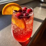 A close-up of a glass filled with vibrant Cranberry Orange Sparkling Punch, garnished with orange slices and fresh cranberries.