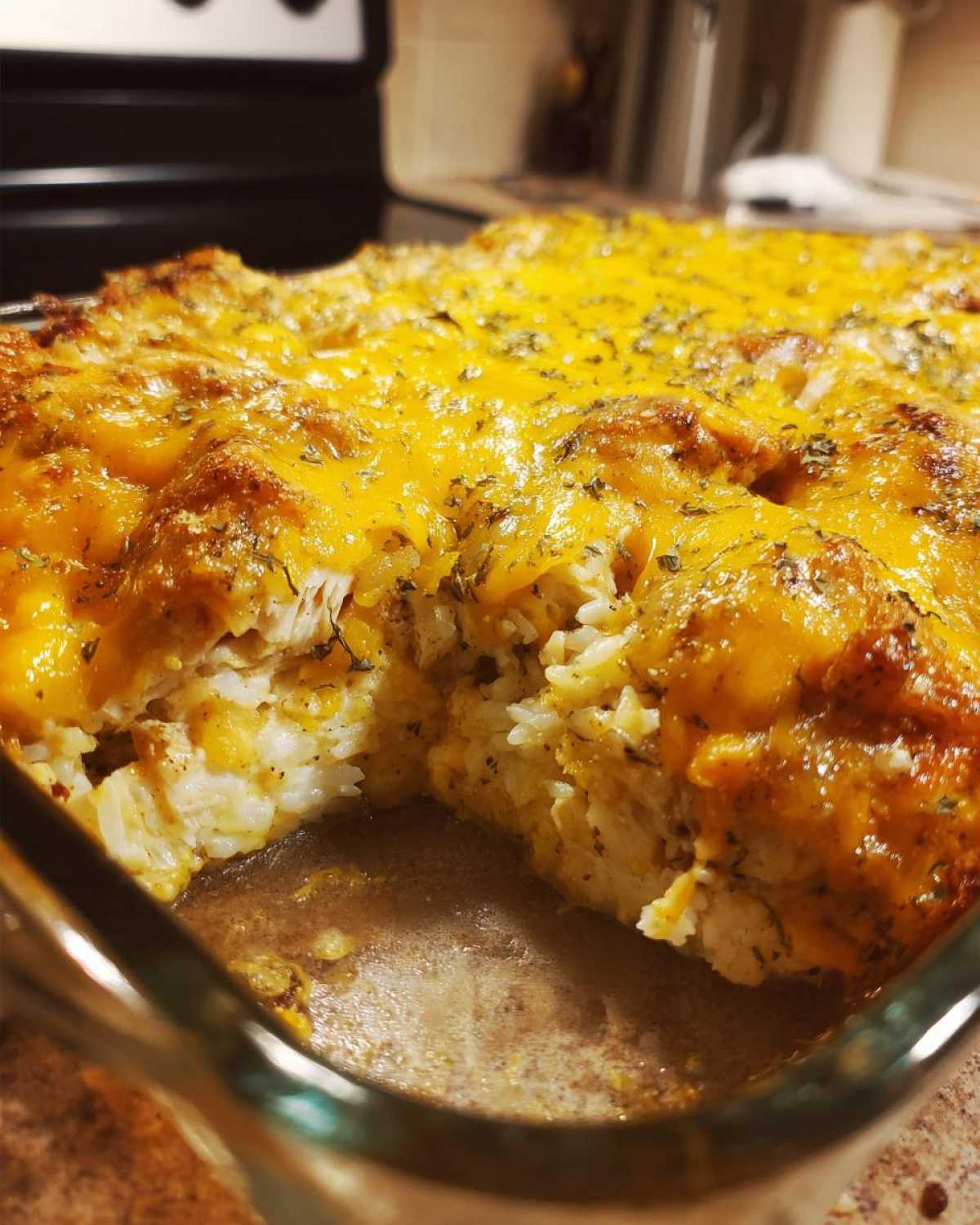 A close-up of a creamy chicken and rice casserole topped with melted cheddar cheese and herbs.