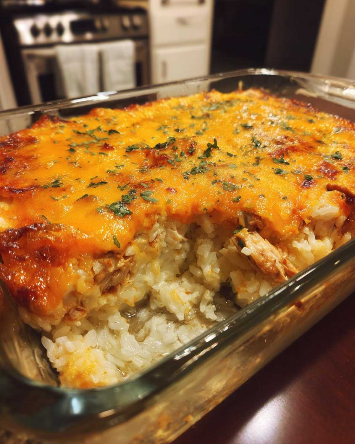 A close-up of a creamy chicken and rice casserole in a glass baking dish, topped with melted cheddar cheese and parsley.