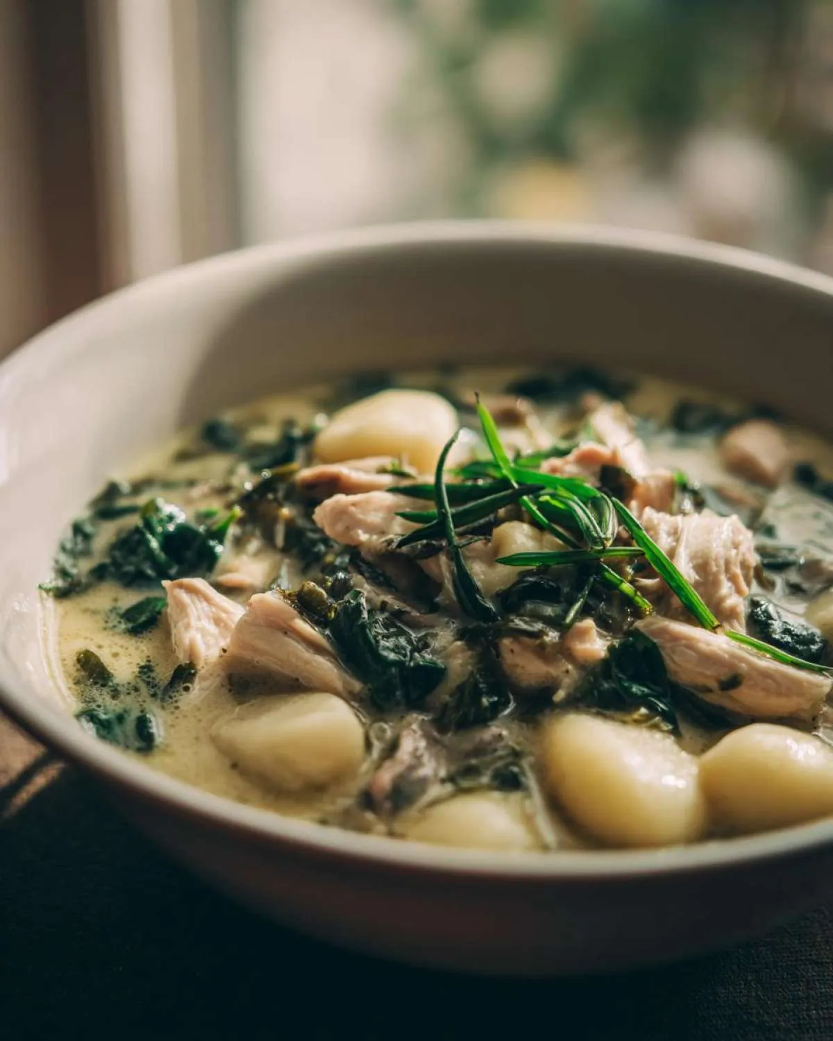 A close-up of a bowl of creamy chicken gnocchi soup, featuring tender chicken pieces, soft gnocchi, and wilted spinach.