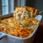 A spoonful of creamy chicken and rice casserole being lifted, showing melted cheese strings and herbs.